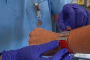 doctor ptting a medical alert bracelet onto a patient, witht he Texa Allergy Logo in the bttom right corner.